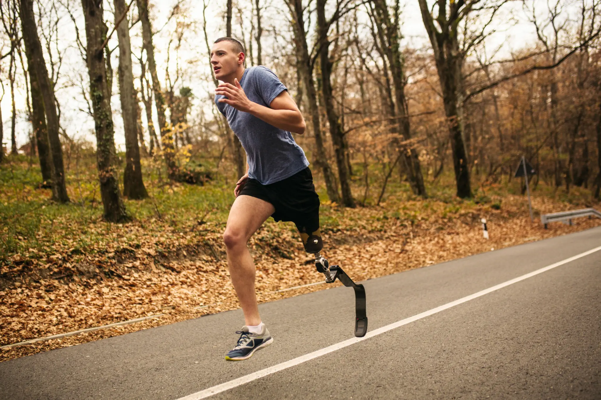 A man with a prosthetic leg running on a forest road.