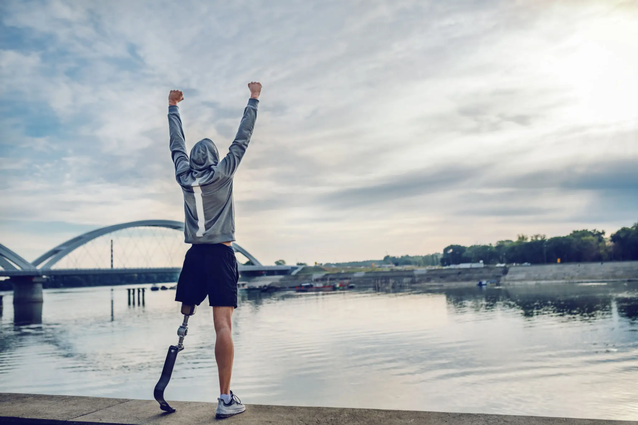 Person celebrating by a river with a bridge in the background.