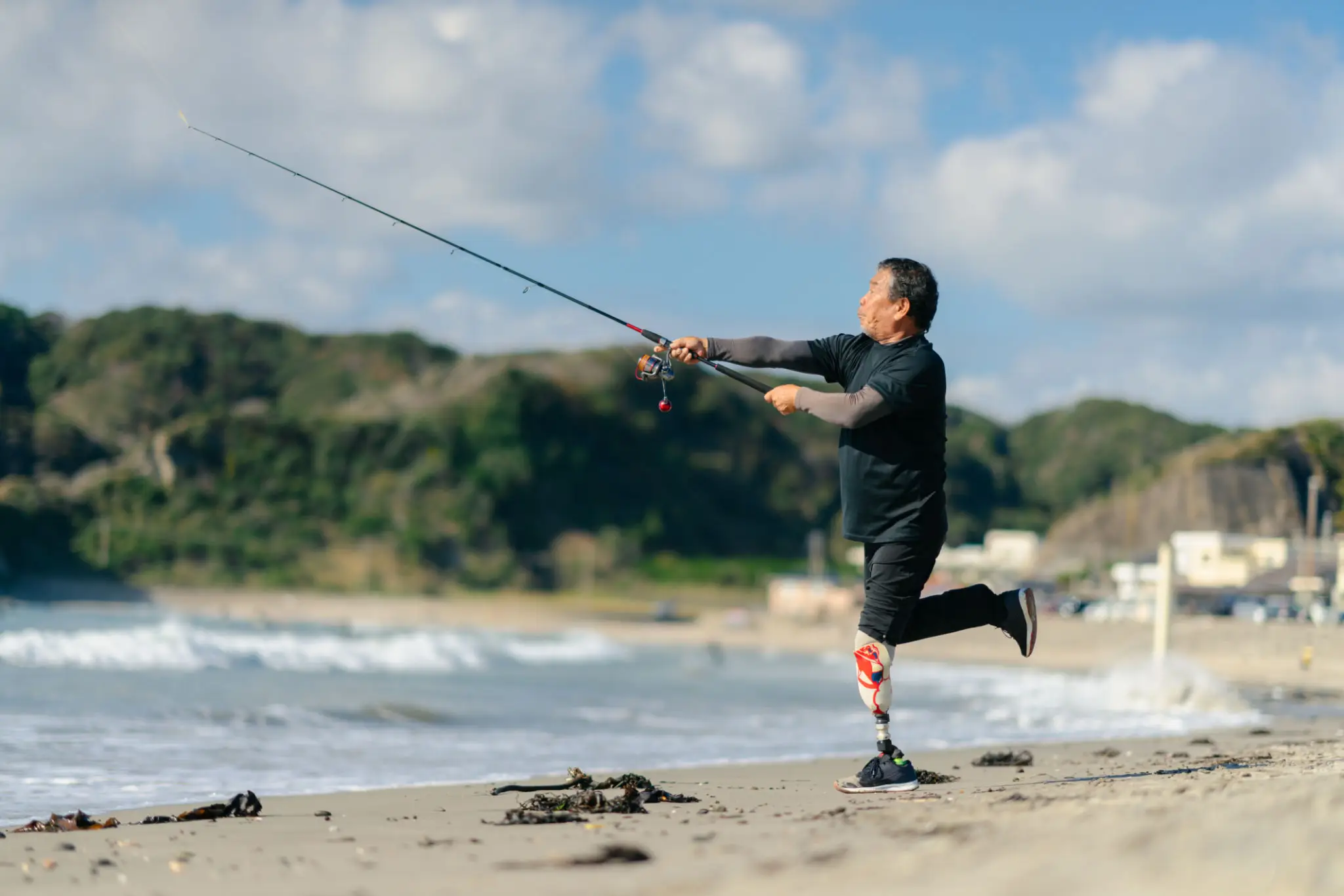 Man with prosthetic leg fishing on a beach.