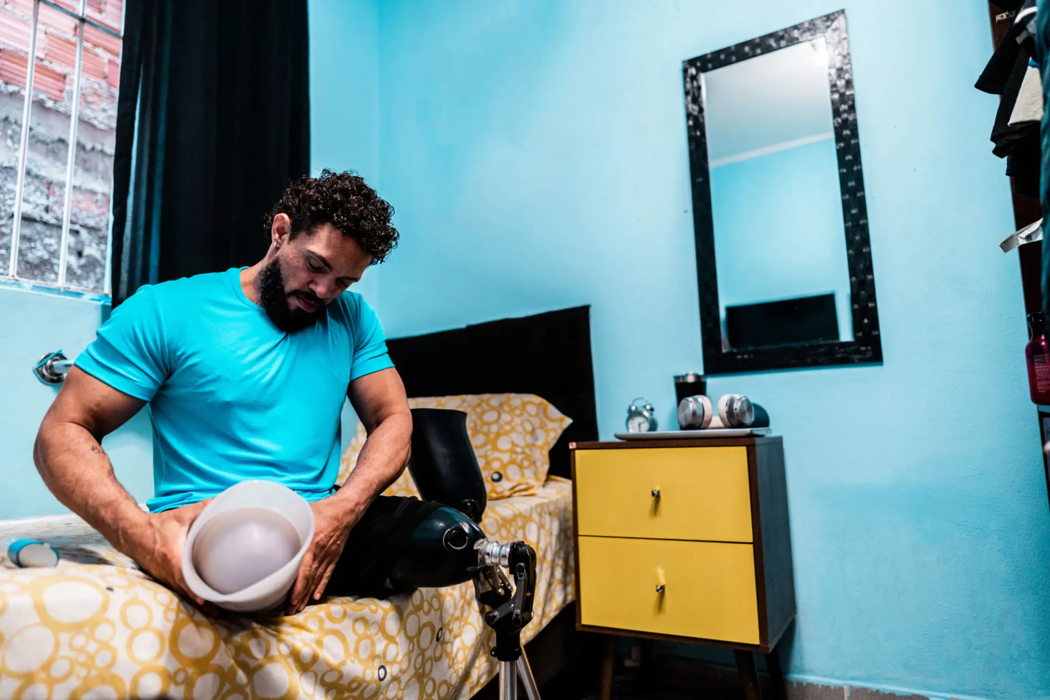 Man sitting on bed while holding a hat and looking down.