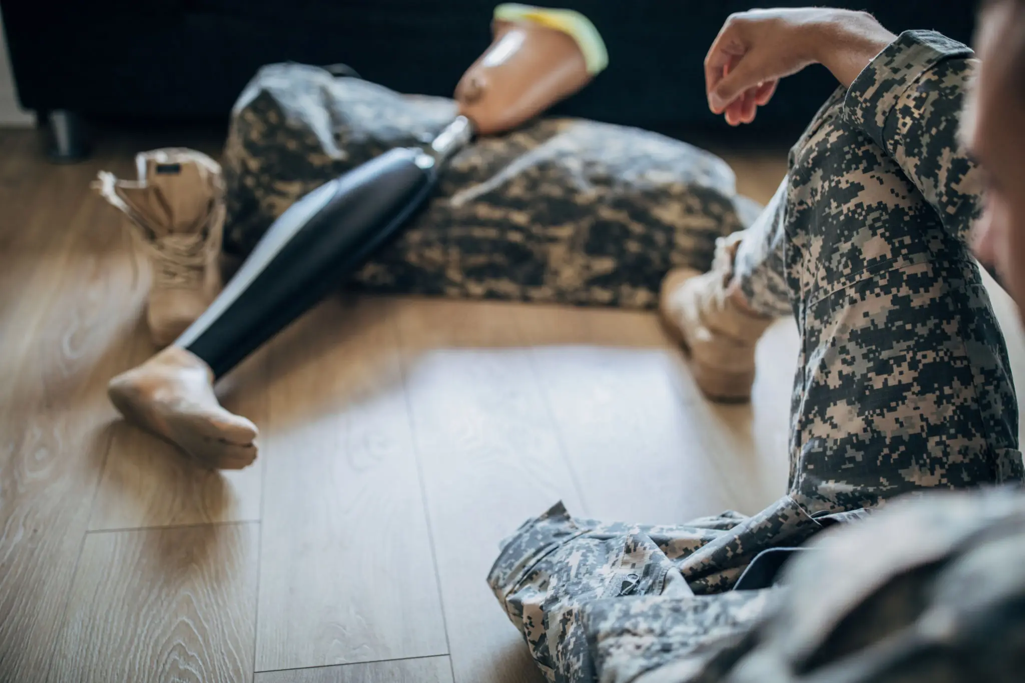 Two people dressed in camouflage uniforms sit on the floor with a rifle.