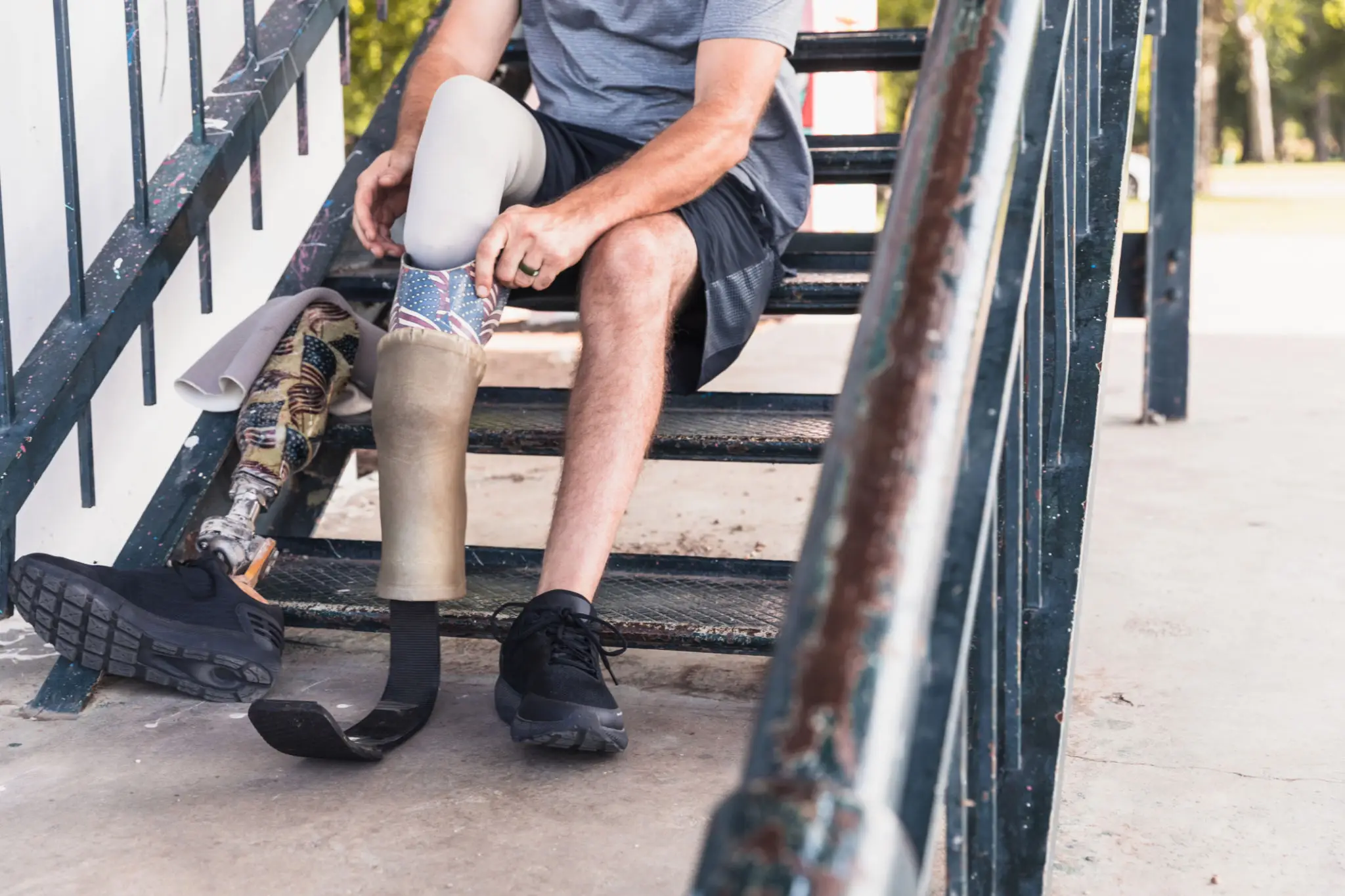 Man with prosthetic leg adjusting it while sitting on stairs.